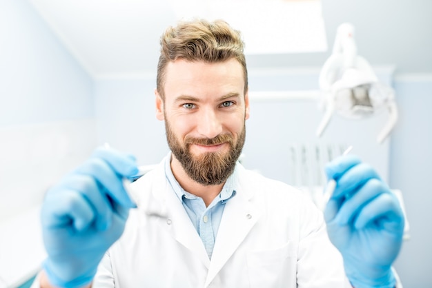 Ritratto di un dentista spaventoso con strumenti dentali che guarda la bocca in telecamera