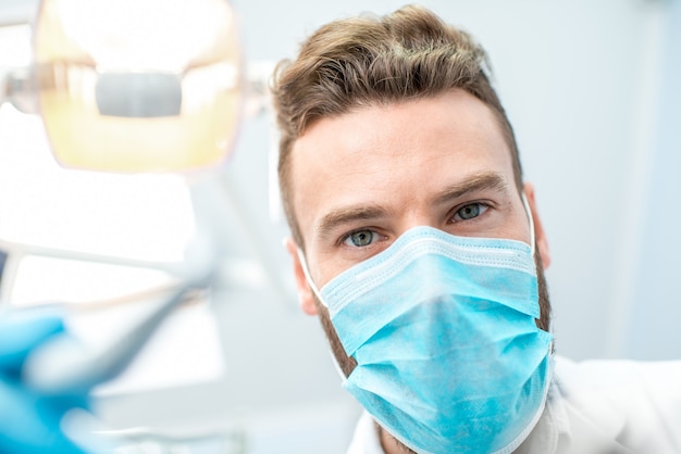 Ritratto di un dentista spaventoso in maschera con strumenti dentali durante l'intervento chirurgico che guarda la telecamera