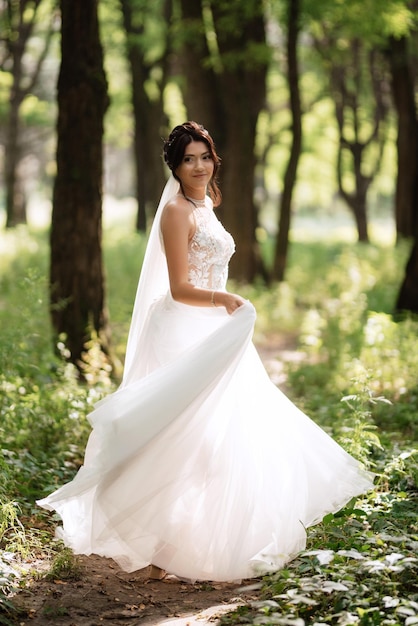 Ritratto di un'elegante ragazza sposa su un sentiero in un bosco di latifoglie con un bouquet