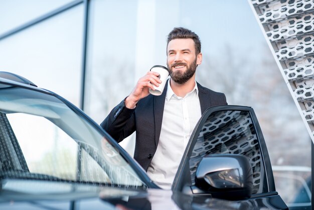 Ritratto di un elegante uomo d'affari in piedi con una tazza di caffè vicino all'auto