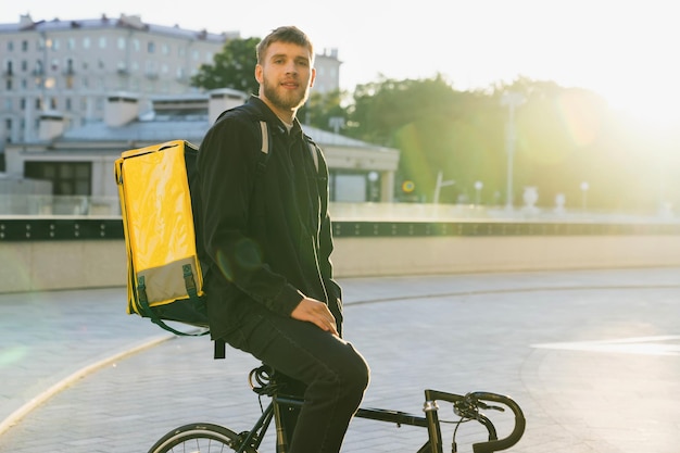 Ritratto di un fattorino della pizza che guarda nella telecamera sullo sfondo di una città moderna Consegna rapida della bici