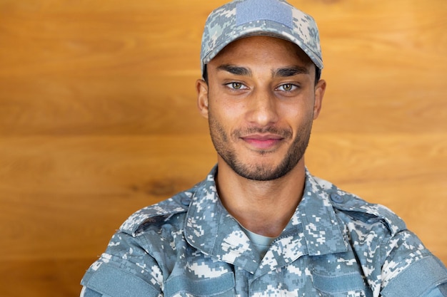 Ritratto di un felice soldato maschio biraciale che indossa l'uniforme militare e il berretto, guardando la telecamera