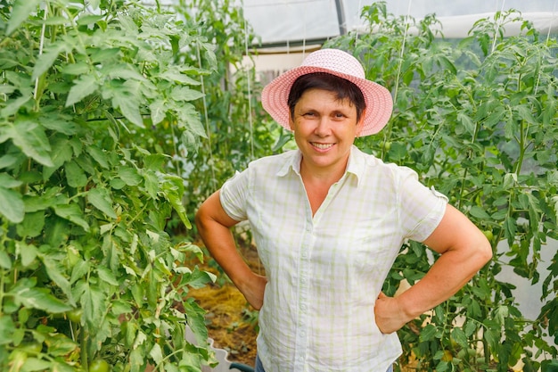 Ritratto di un giardiniere caucasico sorridente con le braccia ai fianchi e il cappello che guarda la telecamera.