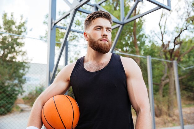 Ritratto di un giocatore di basket barbuto in piedi con la palla all'aperto