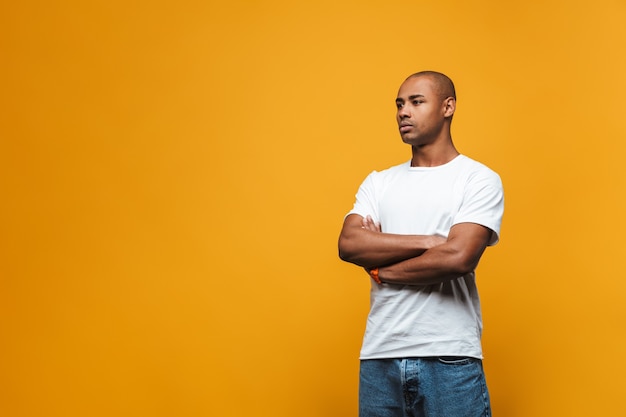 Ritratto di un giovane africano attraente e sicuro di sé in piedi sul muro giallo, con le braccia conserte