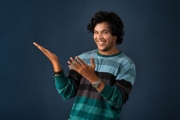 Ritratto di un giovane allegro di successo che punta e presenta qualcosa con la mano o il dito con una faccia sorridente felice