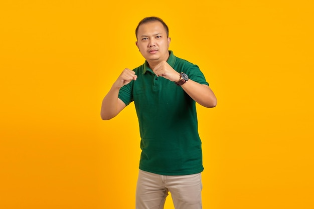 Ritratto di un giovane asiatico arrabbiato che mostra il gesto del pugile su sfondo giallo