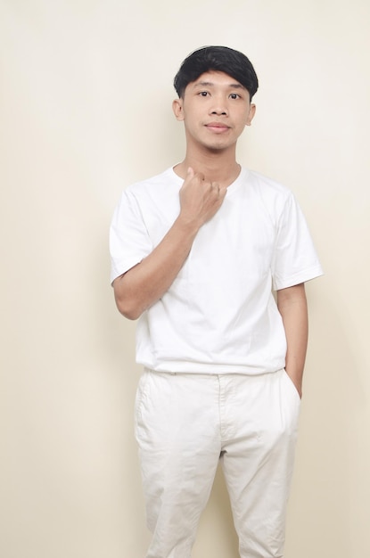 Ritratto di un giovane asiatico in piedi che indossa una maglietta bianca e pantaloni bianchi su sfondo isolato