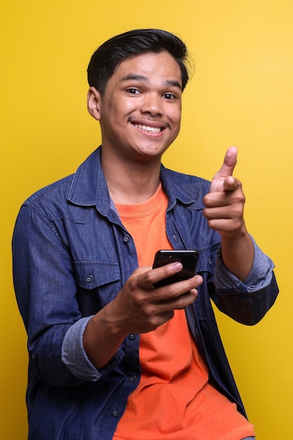 Ritratto di un giovane asiatico sorridente che punta il dito contro la fotocamera mentre tiene il telefono cellulare