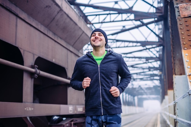Ritratto di un giovane atleta maschio che corre accanto al treno sul ponte del treno durante l'allenamento mattutino.