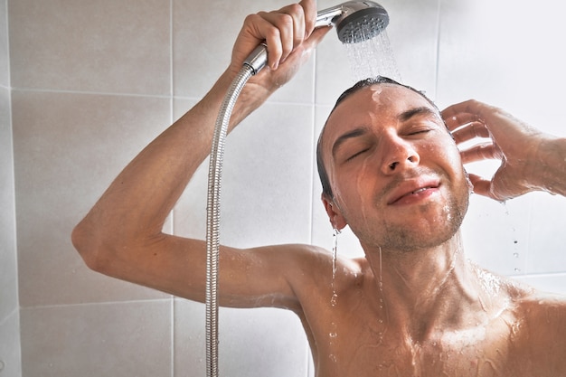 Ritratto di un giovane bell'uomo si lava con il gel doccia, si insapona la testa con lo shampoo nel bagno di casa primo piano