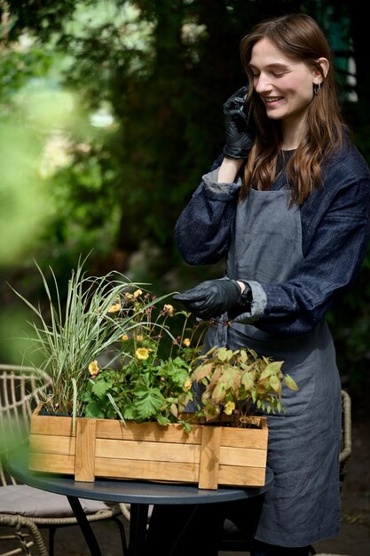 Ritratto di un giovane bellissimo fiorista in grembiule che pianta fiori in un vaso in giardino