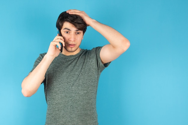 Ritratto di un giovane che parla al telefono cellulare contro il blu.