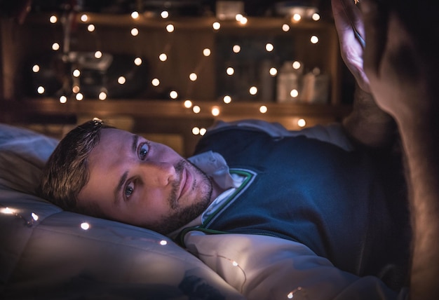 Ritratto di un giovane che usa il cellulare mentre è sdraiato a letto a casa