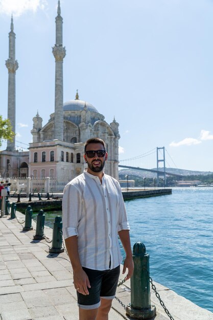 Ritratto di un giovane con barba e occhiali da sole in posa davanti alla moschea ortakoy e al famoso ponte di istanbul