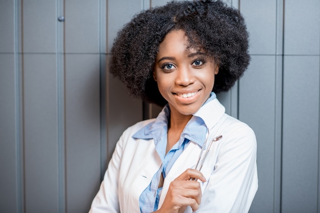 Ritratto di un giovane dentista africano in uniforme sullo sfondo del muro grigio