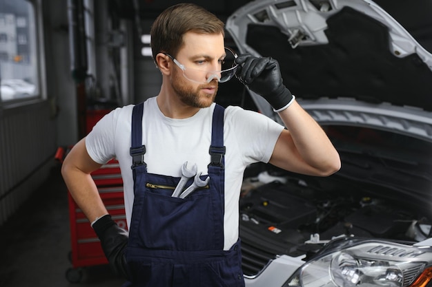 Ritratto di un giovane e bellissimo meccanico di automobili in un'officina automobilistica sullo sfondo del servizio Concetto riparazione di macchine diagnosi guasti riparazione manutenzione tecnica specialistica e computer di bordo