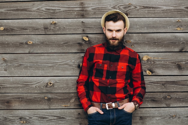 Ritratto di un giovane elegante uomo barbuto vestito in jeans e un vero lavoratore nero dalla camicia rossa.