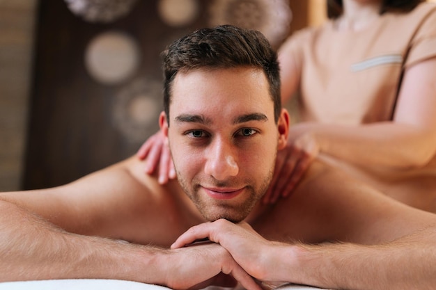 Ritratto di un giovane felice che si rilassa con un massaggio con olio sulla schiena in una stazione termale guardando la telecamera Closeup del viso di un bel maschio che riceve un massaggio alla schiena durante il trattamento del corpo Concetto di stile di vita sano