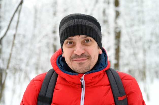 Ritratto di un giovane felice in una giacca rossa e un cappello in una foresta di inverno nevoso