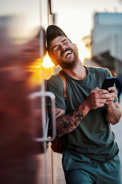 Ritratto di un giovane in tuta che ride per strada con un cellulare in mano