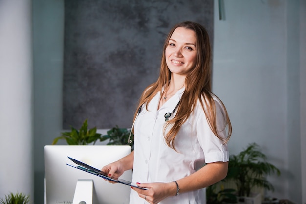 Ritratto di un giovane medico professionista femminile sorridente alla clinica. Primo piano di una roba di medicina in ospedale