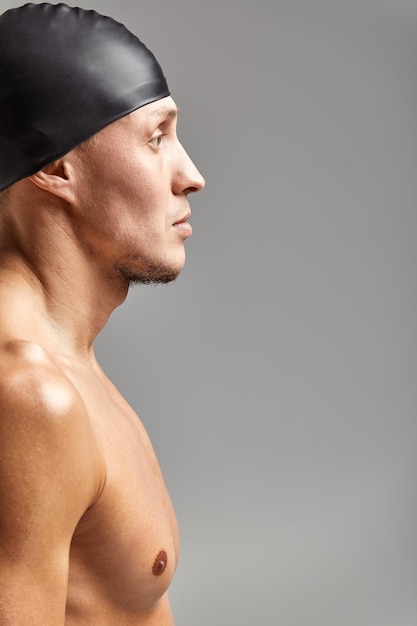Ritratto di un giovane nuotatore che indossa un cappello di gomma in piedi su uno sfondo grigio cappello che si prepara per la vista del profilo di allenamento
