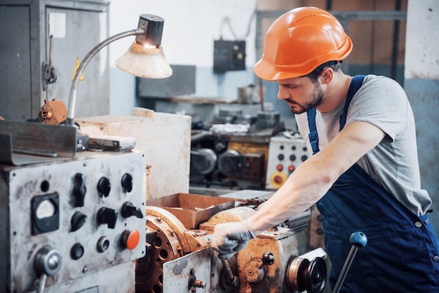 Ritratto di un giovane operaio con un casco rigido in un grande impianto di lavorazione dei metalli L'ingegnere serve le macchine e produce parti per le apparecchiature a gas