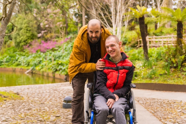 Ritratto di un giovane paralizzato sulla sedia a rotelle spinto da un amico in un parco pubblico cittadino che si diverte in primavera