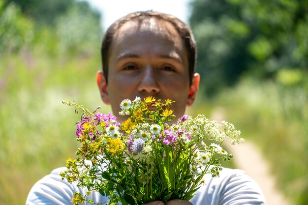 Ritratto di un giovane ragazzo con una maglietta bianca e con un mazzo di fiori in mano Un ragazzo posa sullo sfondo di un campo di fiori e una strada sterrata nel villaggio Il volto di una persona felice