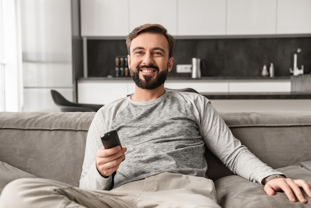 Ritratto di un giovane sorridente che tiene il telecomando della TV