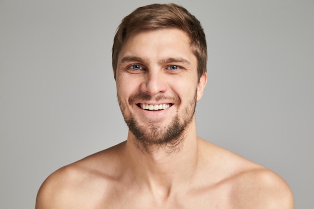 Ritratto di un giovane sorridente con le spalle nude dei nuotatori su uno sfondo grigio potente barba cha