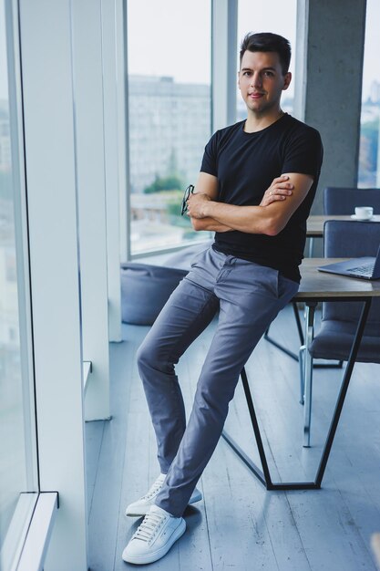 Ritratto di un giovane sorridente in una maglietta nera sullo sfondo di un ufficio moderno Ragazzo alla moda in abiti casual