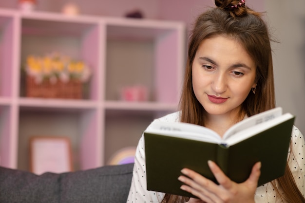 Ritratto di un giovane studente che legge un libro. Bella giovane donna castana che legge un libro sul letto a casa