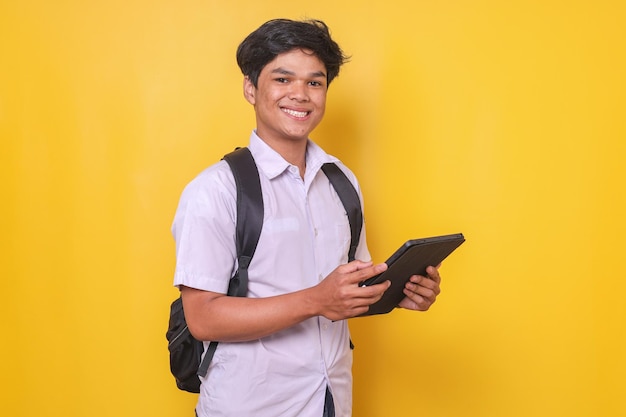 Ritratto di un giovane studente maschio asiatico intelligente in uniforme scolastica che guarda la telecamera sorridendo mentre tiene