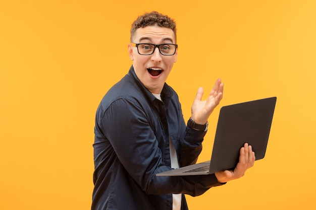 Ritratto di un giovane stupito con gli occhiali che tiene in mano e usa un portatile
