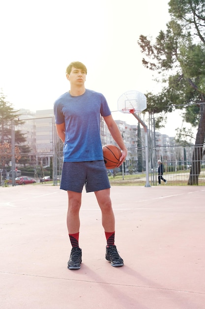 Ritratto di un giovane su un campo da basket in possesso di un'immagine verticale di basket