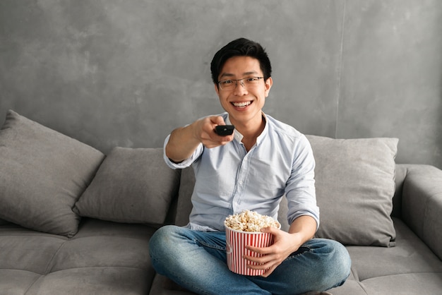 Ritratto di un giovane uomo asiatico sorridente che tiene popcorn