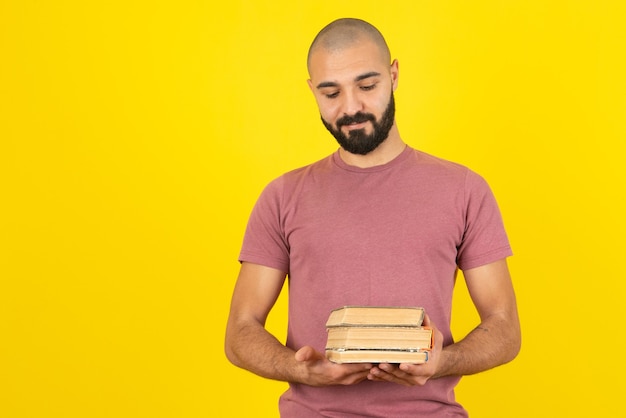Ritratto di un giovane uomo barbuto che tiene libri sul muro giallo.