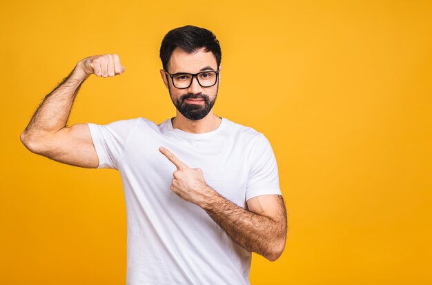 Ritratto di un giovane uomo barbuto felice vestito di t-shirt che mostra bicipiti isolate su sfondo giallo.