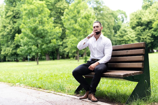 Ritratto di un giovane uomo d'affari fisicamente in forma fuma sigaro cubano nel parco