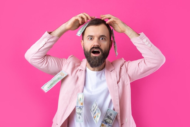 Ritratto di un giovane uomo d'affari soddisfatto con la barba vestito con una giacca rosa che ci mostra le banconote in dollari su uno sfondo rosso dello studio Gusto odore di denaro