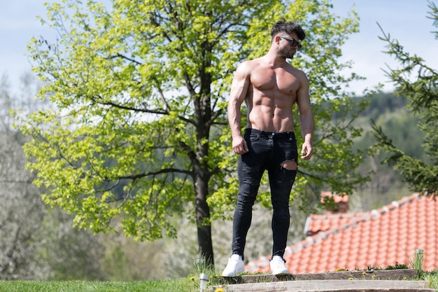 Ritratto di un giovane uomo fisicamente in forma che mostra il suo corpo ben allenato mentre indossa jeans neri Muscoloso atletico bodybuilder Modello di fitness in posa dopo gli esercizi all'aperto un posto per il tuo testo