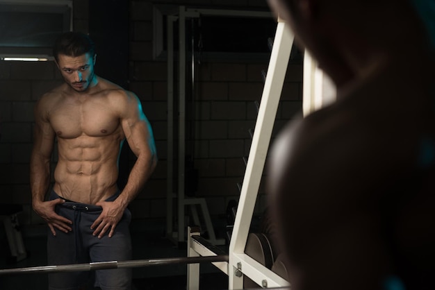 Ritratto di un giovane uomo fisicamente in forma che mostra il suo corpo ben allenato modello di fitness bodybuilder atletico muscolare in posa dopo gli esercizi