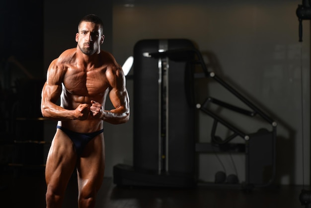 Ritratto di un giovane uomo fisicamente in forma che mostra il suo corpo ben allenato modello di fitness bodybuilder atletico muscolare in posa dopo gli esercizi