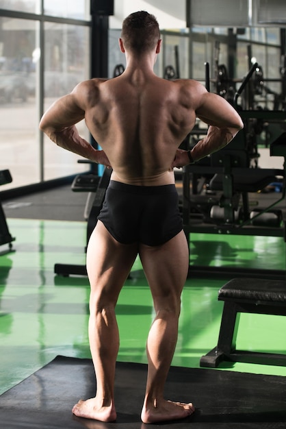 Ritratto di un giovane uomo fisicamente in forma che mostra il suo corpo ben allenato modello di fitness bodybuilder atletico muscolare in posa dopo gli esercizi