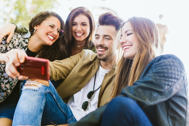 Ritratto di un gruppo di amici che scattano foto con il cellulare in strada.