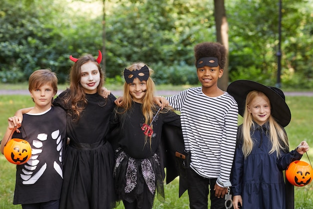 Ritratto di un gruppo multietnico di bambini che indossano costumi di Halloween stando in piedi all'aperto e