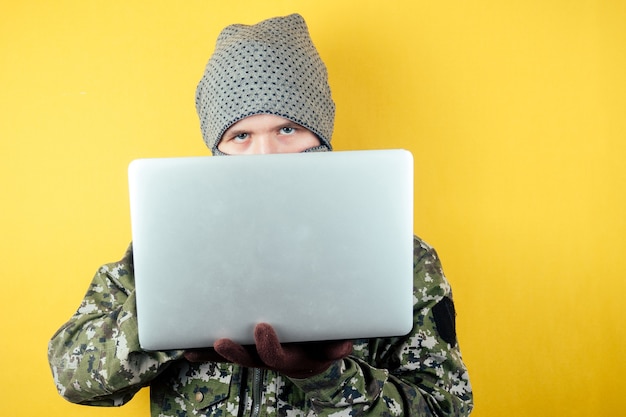 Ritratto di un hacker uomo terroris in un camuffamento e una maschera sta guardando il laptop.