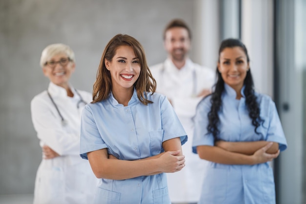 Ritratto di un'infermiera sorridente in piedi con le braccia incrociate in un corridoio dell'ospedale con i suoi colleghi sullo sfondo.